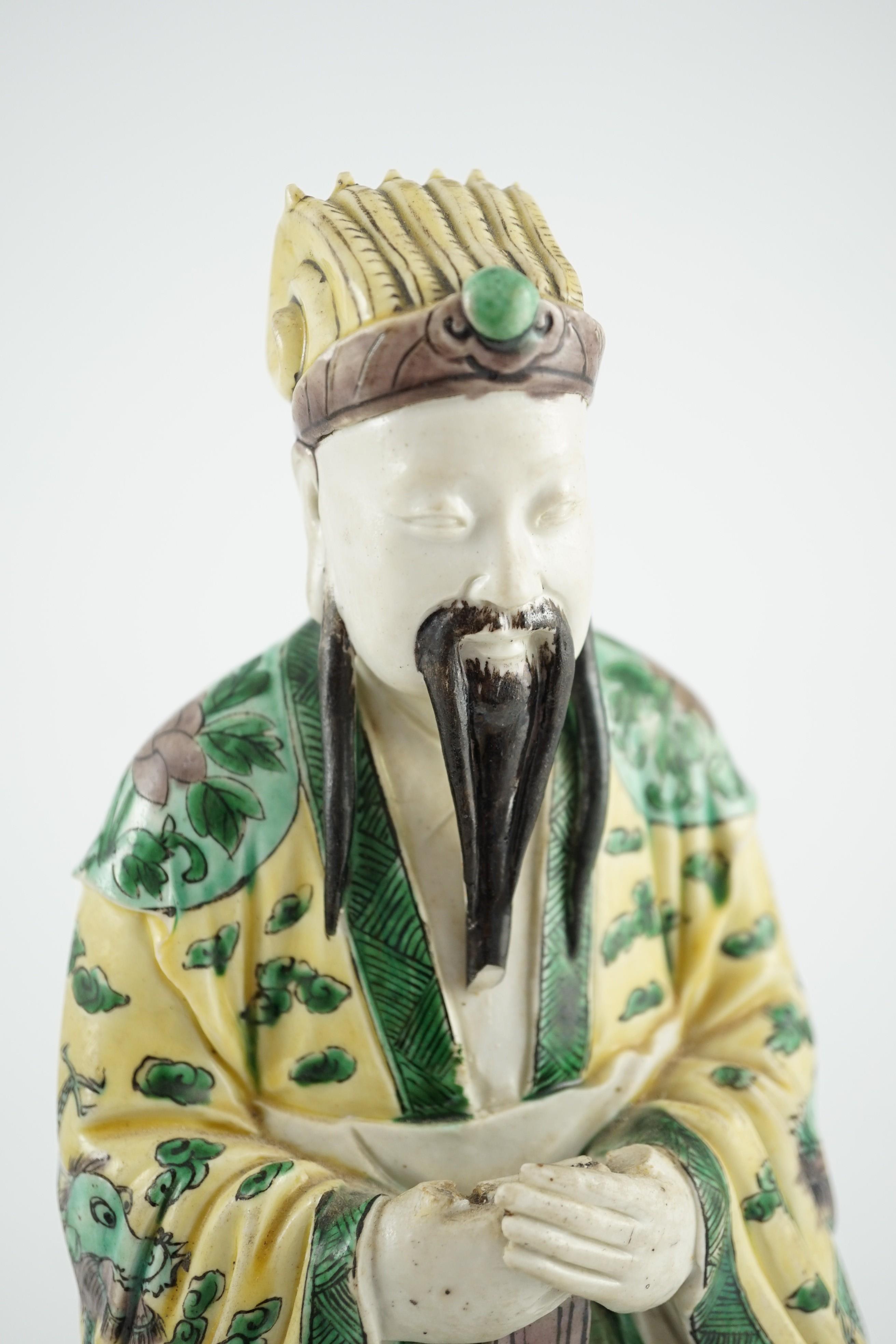 A Chinese enamelled biscuit figure of a seated court official, Kangxi period, 31.5cm high, small losses